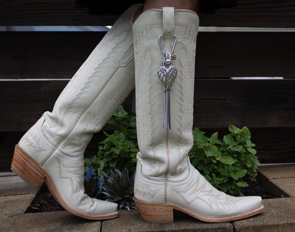 White knee-high boots with a decorative heart charm hanging on the side.