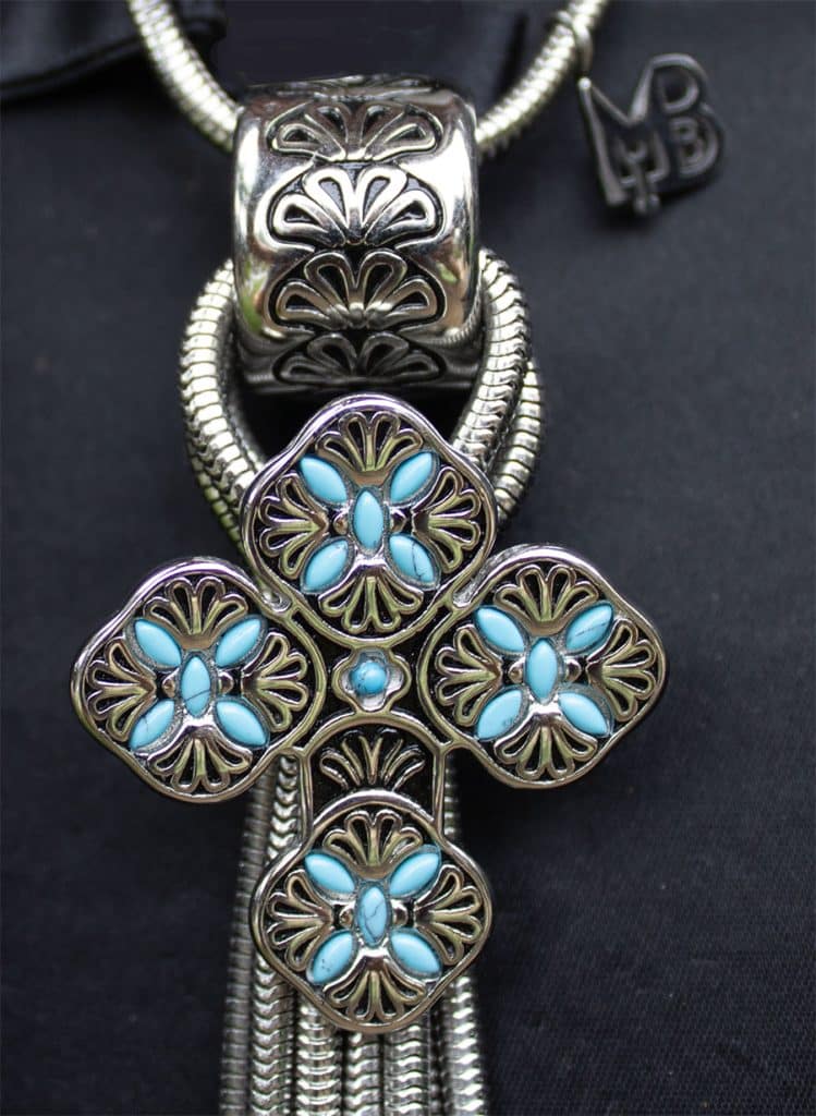 Close-up of a silver pendant with turquoise stones arranged in floral patterns.
