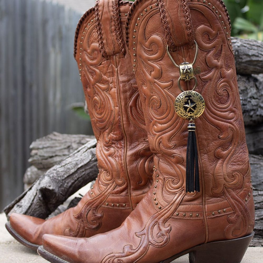 Intricately tooled brown leather cowboy boots with decorative charms.